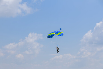 Naklejka na ściany i meble Skydiver with yellow and blue parachute against blue sky having fun in the air, sports aerial entertainment. Air sports.