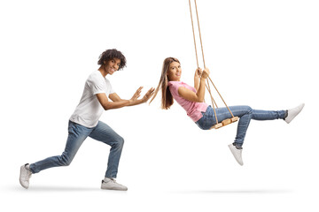Young african american guy pushing a caucasian female on a swing - obrazy, fototapety, plakaty