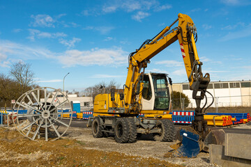 Yellow excavator at a construction site next to an empty cable drum. Blue sky with light clouds.