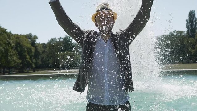 Carefree Young Man Standing in water fountain chilling in summer time