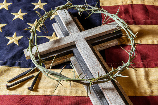 wooden cross and crown of thorns on American flag with rose head nails