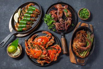 Set of Seafood Dishes. Crabs, octopus, squids and tiger shrimps on cast iron pans and plates on a black background. Top view.