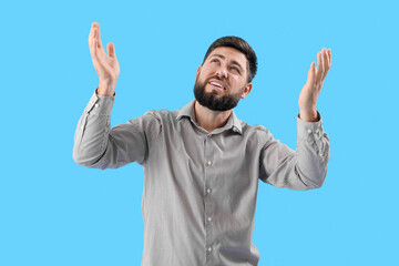 Stressed young man suffering from loud noise on blue background