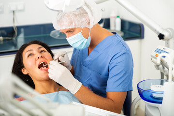 Dentist and asian woman patient sitting in medical chair during checkup at dental clinic office