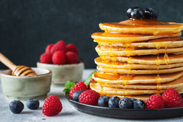 Delicious pancakes, with fresh blueberries, raspberry and maple syrup or honey on a dark background