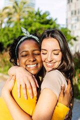 Vertical portrait of candid happy multiracial best women friends embracing outdoors. Close up view...