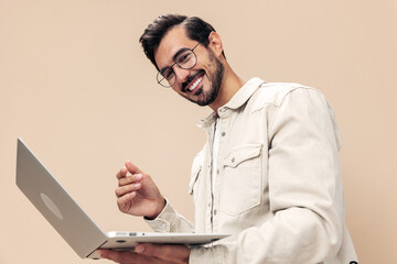 Portrait of a stylish man smile with teeth with a laptop in the hands of a freelancer, on a beige background in a white t-shirt, fashionable clothing style, space space