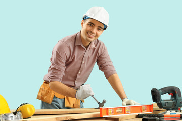 Young carpenter with hammer and wooden planks at table on blue background