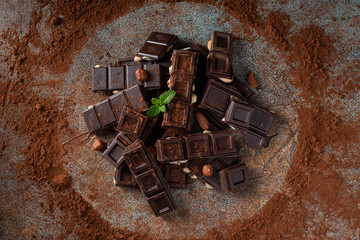 Dark and milk chocolate with nuts on a dark background sprinkled with cocoa powder.