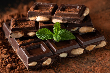 Dark and milk chocolate with nuts on a dark background sprinkled with cocoa powder.