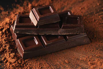 Dark and milk chocolate with nuts on a dark background sprinkled with cocoa powder.