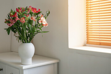 Vase with beautiful alstroemeria flowers on chair near light wall