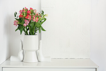 Vase with bouquet of beautiful alstroemeria flowers and picture on table against light wall