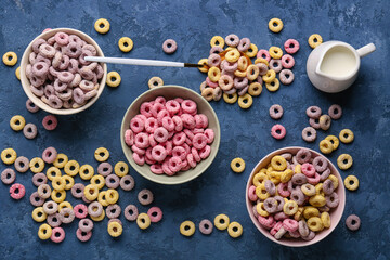 Bowls of colorful cereal rings and pitcher with milk on blue grunge background