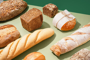Loaves of different fresh bread on green table