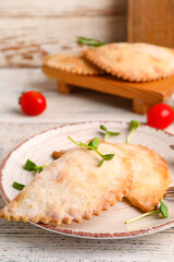 Plate with baked meat empanadas on light wooden table, closeup
