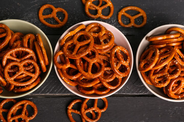 Bowls with tasty pretzels on dark color background, closeup