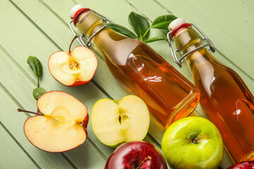 Glass bottles of fresh apple cider vinegar and fruits on green wooden background