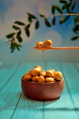 Spoonful of flavor - green olives with olive oil spilling over wooden bowl filled with olives