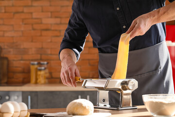 Man making pasta with machine at table in kitchen, closeup