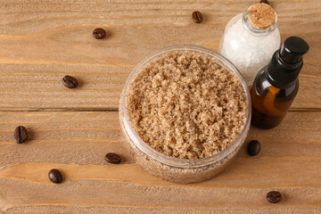 Jar of body scrub, sea salt, essential oil and coffee beans on wooden background
