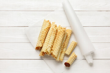 Parchment with delicious wafer rolls on white wooden background