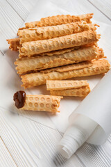 Parchment with delicious wafer rolls on white wooden background
