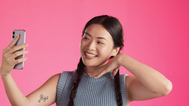 Asian woman, face and smile for selfie, vlog or profile picture against a pink studio background. Happy Japanese female smiling for photo with facial expression and hand signs for social media post