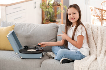 Little girl pointing at record player on sofa at home