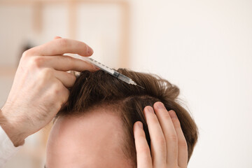 Young man with injection for hair growth in bathroom, closeup