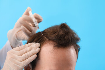 Young man receiving injection for hair growth on blue background, closeup