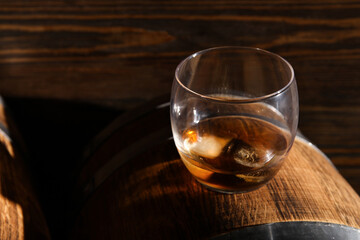 Glass of cold whiskey on barrel against wooden background wooden background