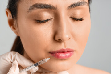 Young woman receiving filler injection in face against grey background, closeup