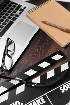 Laptop with eyeglasses, movie clapper and notebook on dark wooden background, closeup