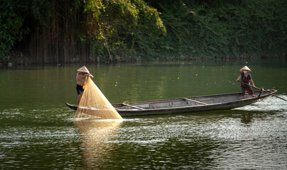 Vietnamese fishermen catching fish and throwing out two large yellow fishnet on a boat from the peaceful Nhu Y river in Hue city, Vietnam