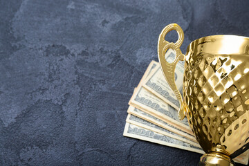 Gold cup with money on dark background, closeup