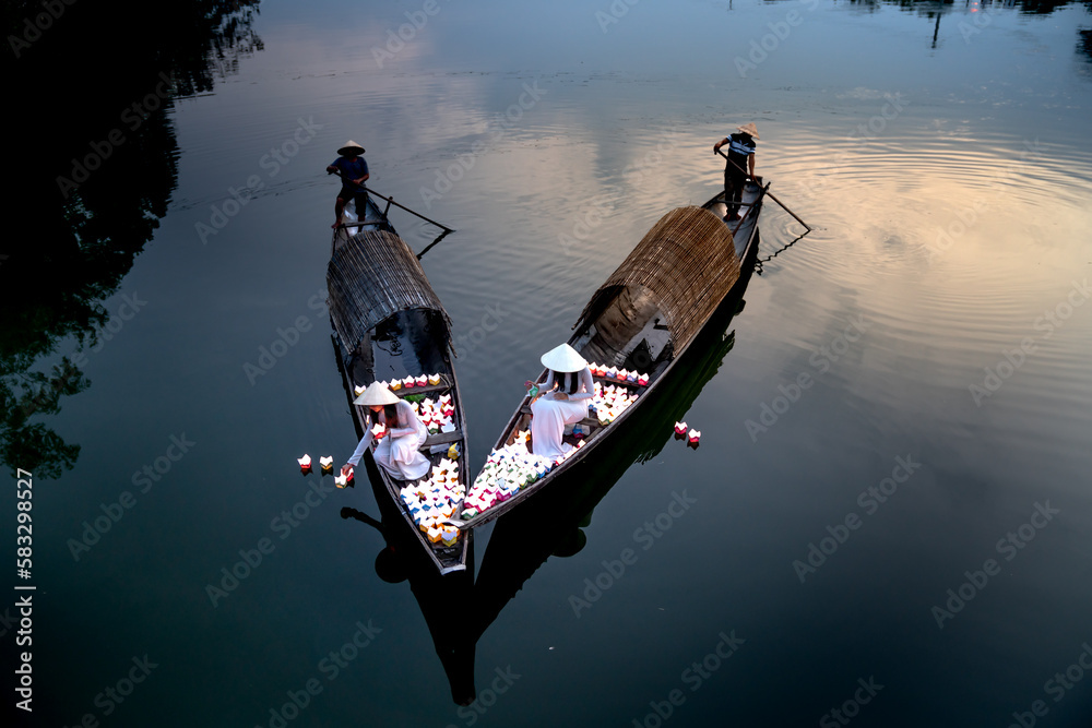 Wall mural Two Vietnamese girls with wihte tradition Ao Dai are lighting candle in lantern to pray in the river in Hue City, Vietnam - Ao dai is famous traditional costume for the women in Vietnam.