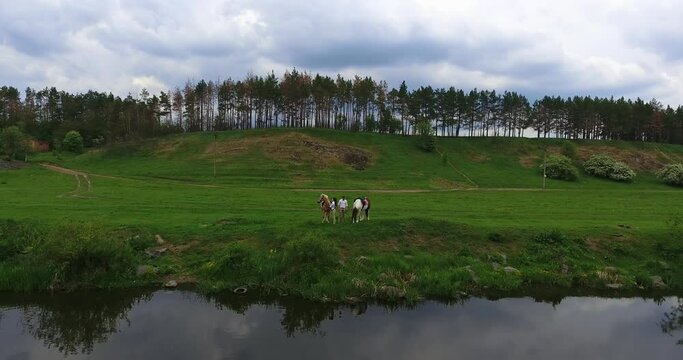 Cloudy summer day in the nature. Couple holding horses stands at the river bank. Top view.