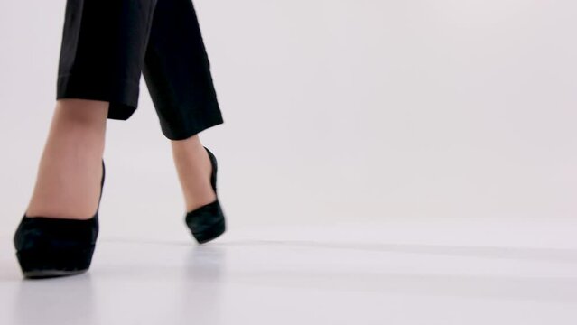 women's legs in high heels in shoes walk along white hall background short black pants Girl walking in black shoes down view. High quality 4k footage