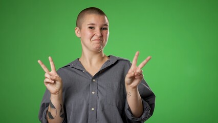Portrait of happy gender fluid non binary young woman 20s smiling and giving peace or victory sign...
