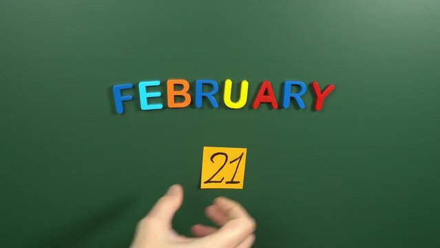 Hand sticking a sticker 21 February calendar day on school board. 21 date of February. Twenty first day of February. 21th date number. 21 day calendar. Twenty one date