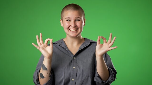 Portrait of young non binary gender fluid woman 20s giving okay gesture smiling happy isolated on green screen background studio portrait