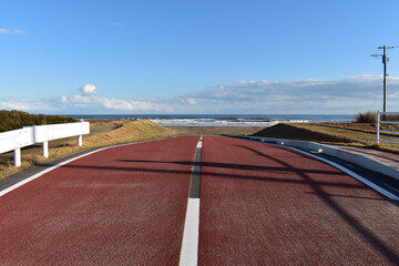 青い空白い雲、坂道の向こうに海が広がる道路です。