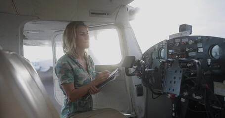 Woman pilot in military uniform pre-flight checking inside on a small aviation airplane. Flight pre-check inspection. - Powered by Adobe
