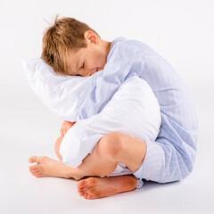 Young preteen boy wearing pajamas sitting on the studio floor holding pillow © 3Days2Go Media