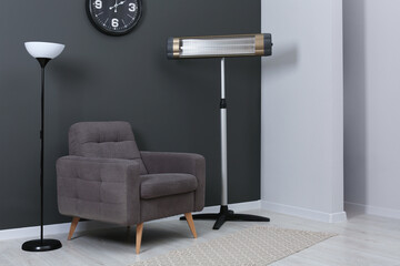 Electric infrared heater and stylish armchair in room
