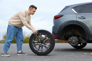 Fototapeta na wymiar Young man changing tire of car on roadside