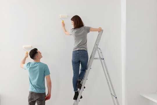 Young man and woman painting wall with rollers indoors. Room renovation