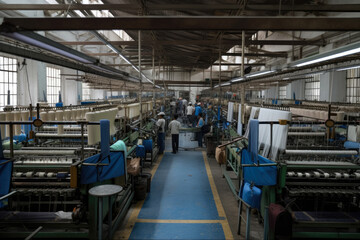 A textile weaving factory with workers operating looms to produce woven fabrics and textiles, generative ai