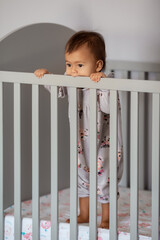 Infant baby girl  standing in crib at daytime, babyhood and childhood memories concept